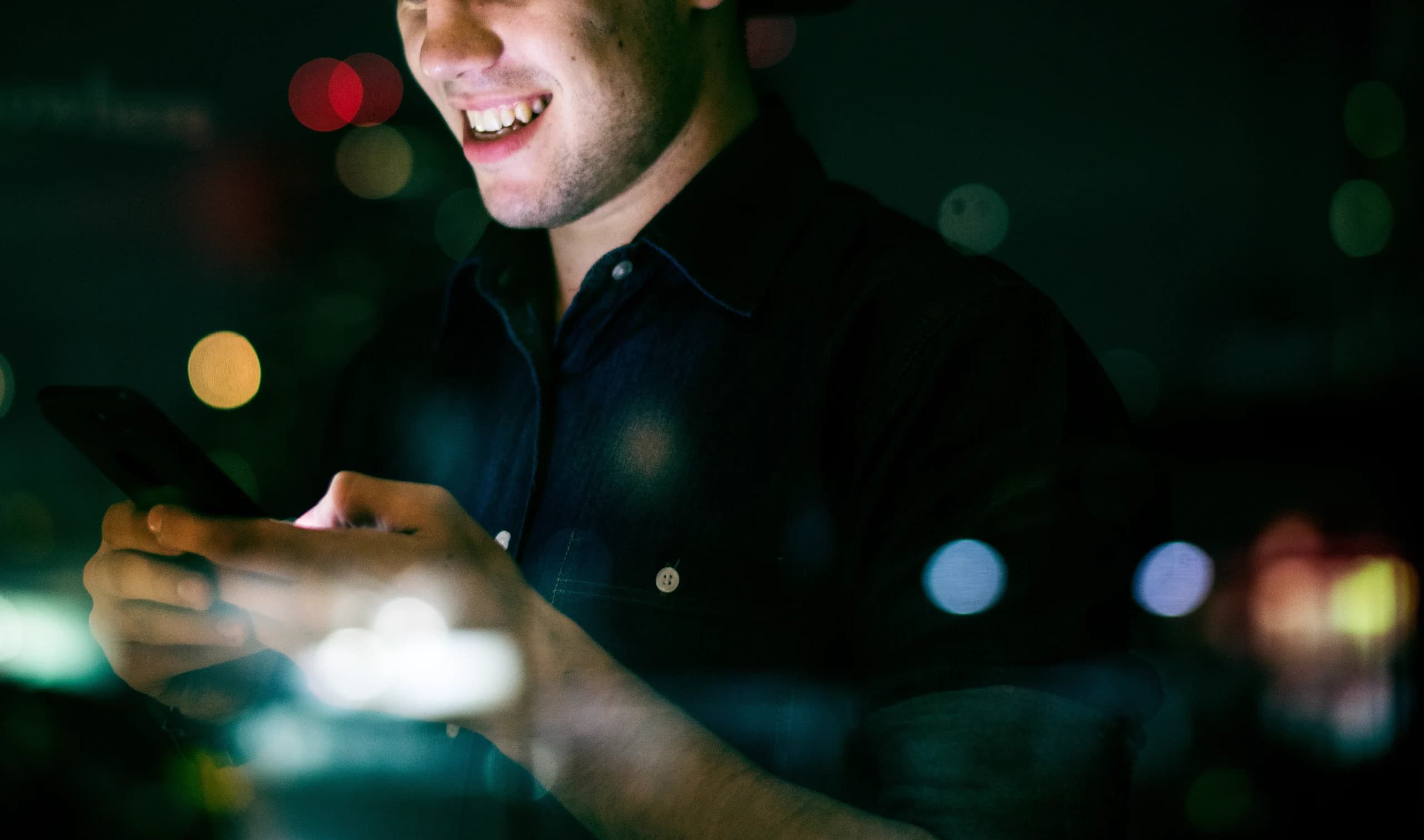 happy-young-adult-male-using-smartphone-night-cityscape